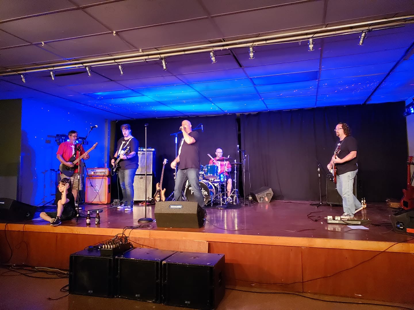 A six-piece band playing on the hall stage under blue stage lighting