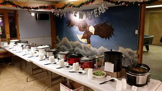 A buffet line of slow cookers laid out along tables in front of the eagle mural, decorated for New Year