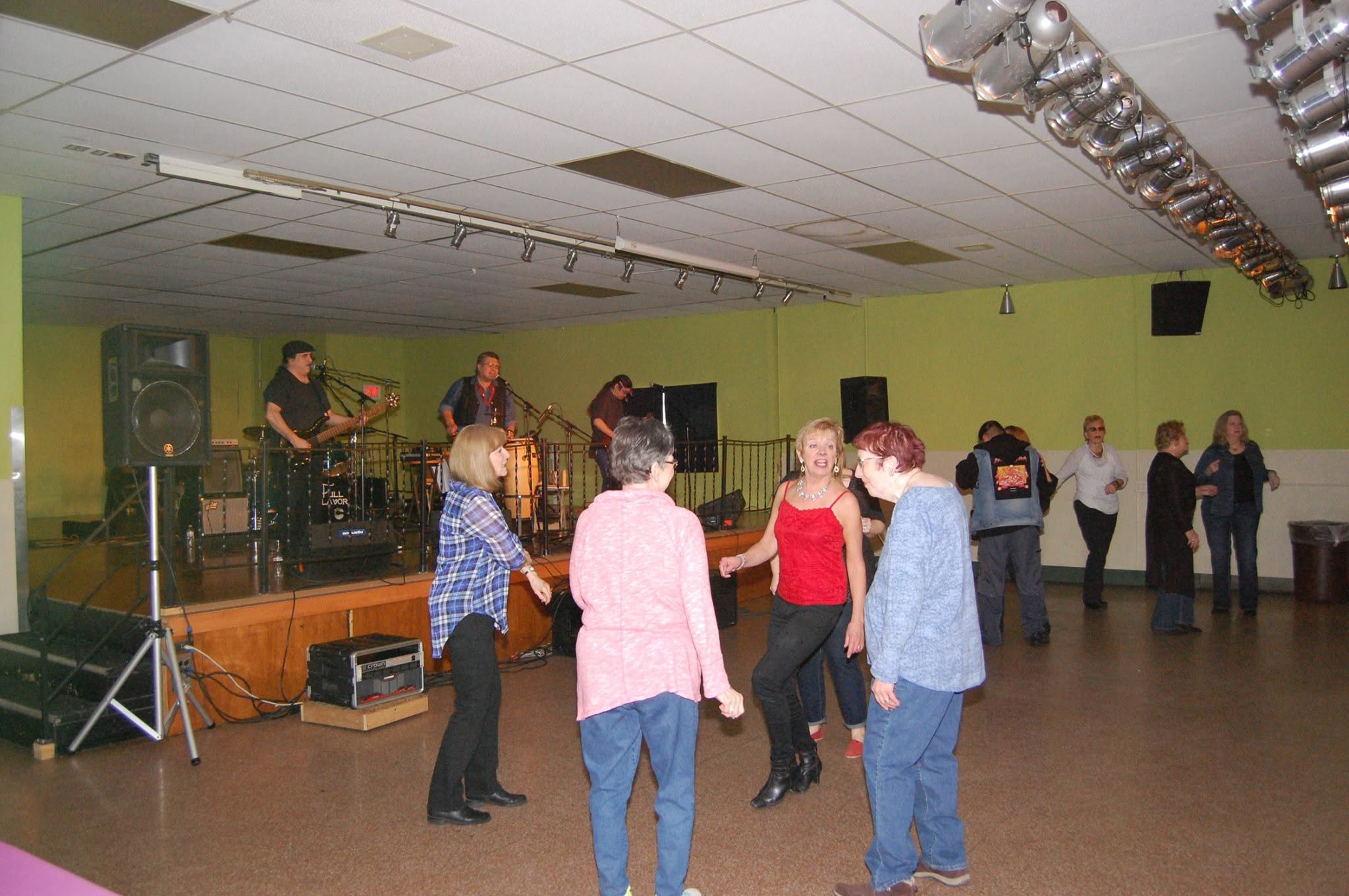 Members dancing on the hall floor while a band plays on the stage behind them