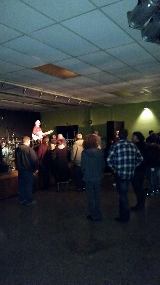 Members standing together watching a guitarist play in the upper hall